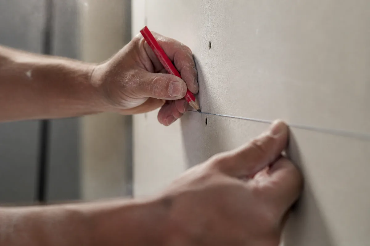 Mains d&rsquo;un artisan traçant un repère sur une cloison en cours de pose